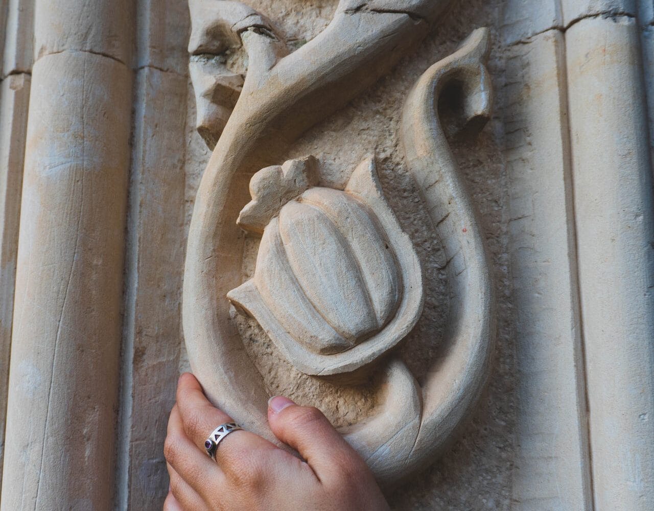 Close-up of a person touching an ornate floral stone carving on the wall of an abandoned Soviet-era sanatorium in Tskaltubo, Georgia, highlighting intricate architectural details and cultural heritage