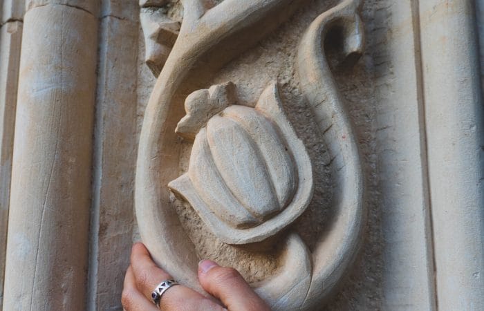 Close-up of a person touching an ornate floral stone carving on the wall of an abandoned Soviet-era sanatorium in Tskaltubo, Georgia, highlighting intricate architectural details and cultural heritage