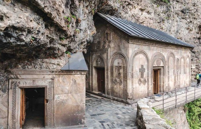 Mghvimevi Monastery in Chiatura, Georgia, a historic rock-carved Orthodox monastery nestled into a cliffside, surrounded by lush greenery and reflecting centuries of Georgian religious architecture