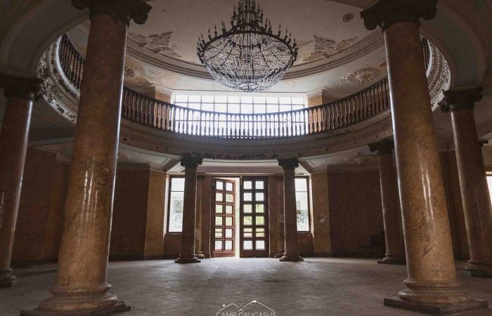 Interior of abandoned Tskaltubo sanatorium with neoclassical columns, chandelier, and Stalin-era Soviet architecture