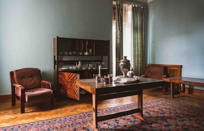 Decaying room with a vintage wooden table and scattered belongings inside an abandoned Soviet-era sanatorium in Tskaltubo, Georgia, reflecting the remnants of Stalinist architecture and forgotten history