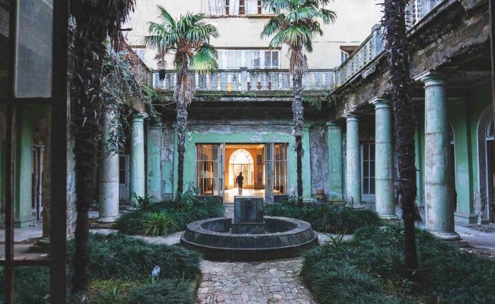 Abandoned courtyard of a Soviet-era sanatorium in Tskaltubo with palm trees, a central fountain, and surrounding columns