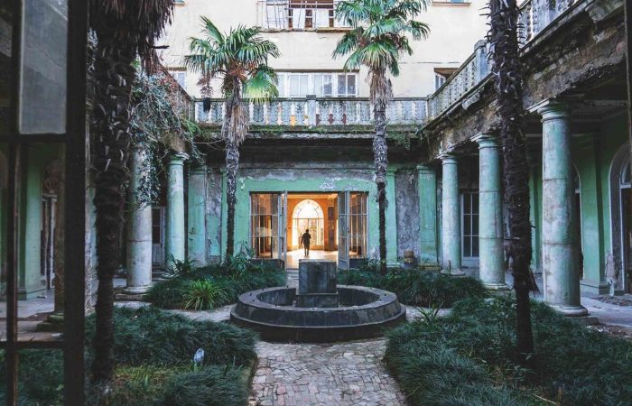 Abandoned courtyard of a Soviet-era sanatorium in Tskaltubo with palm trees, a central fountain, and surrounding columns