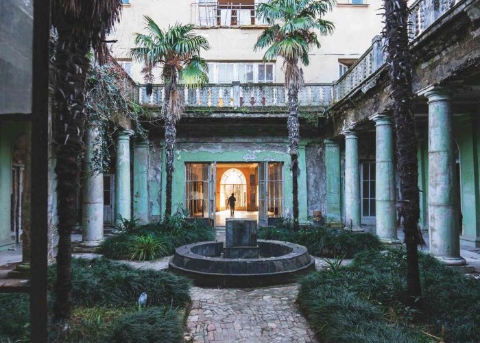 Abandoned courtyard of a Soviet-era sanatorium in Tskaltubo with palm trees, a central fountain, and surrounding columns