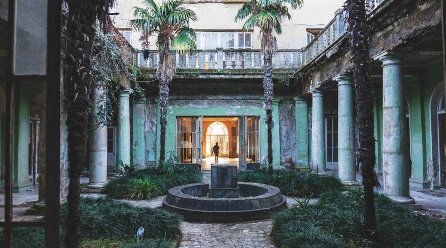 Abandoned courtyard of a Soviet-era sanatorium in Tskaltubo with palm trees, a central fountain, and surrounding columns