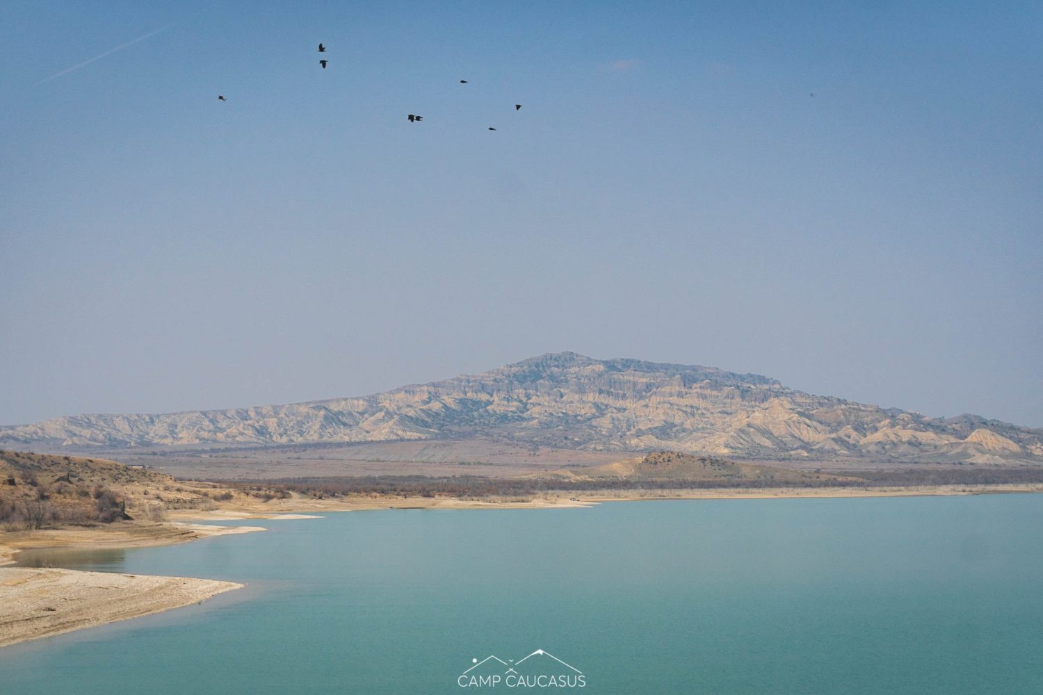 Birds flying over Dali Mountain and turquoise reservoir in Vashlovani National Park, Georgia