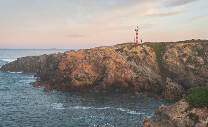 Sunset over cliffs and lighthouse on the Fisherman’s Trail near Porto Covo, Portugal.